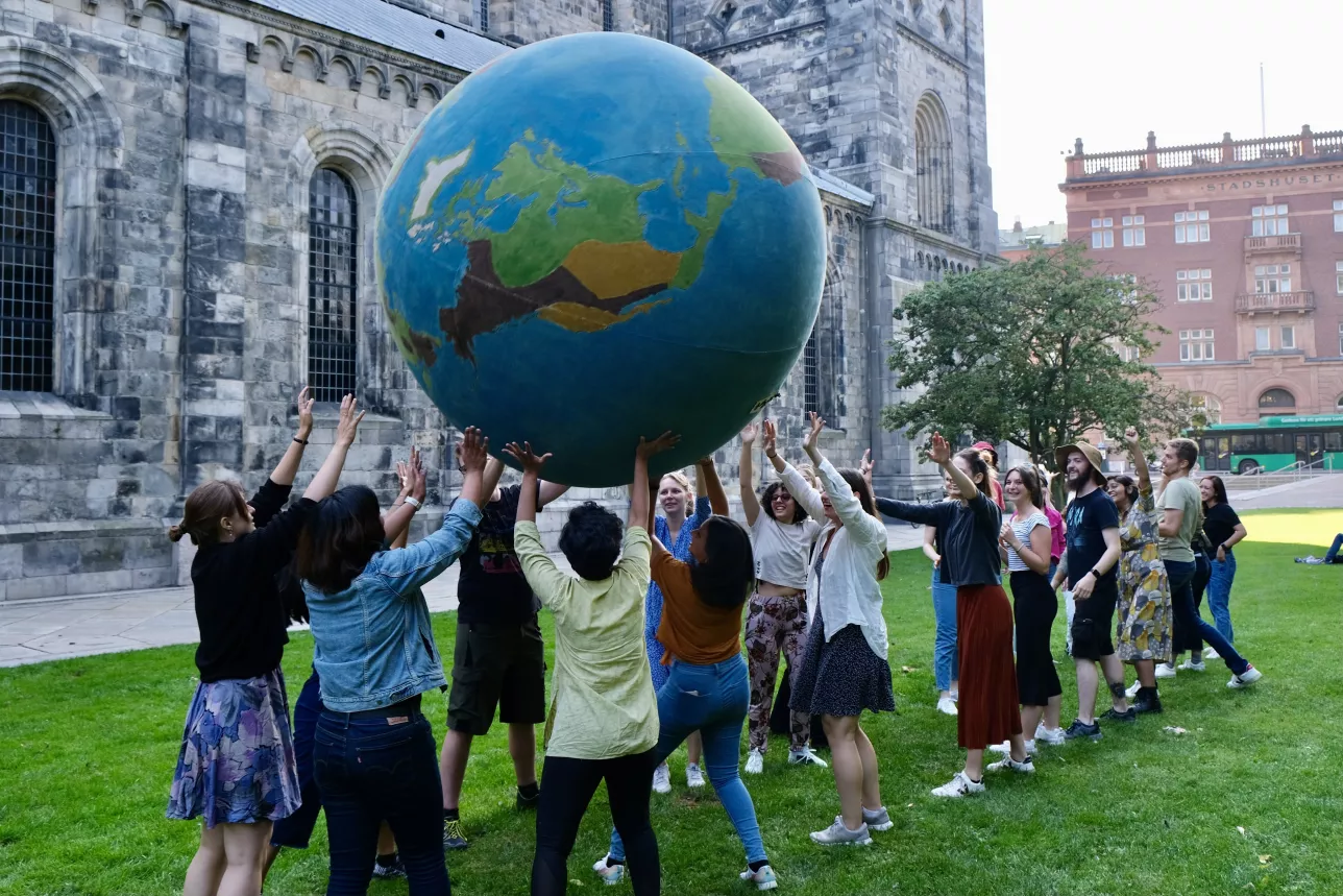 Students holding a giant ball looking like the earth in front of the cathedral of Lund. Photo. 