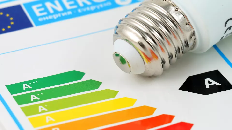 Colourful arrows showing energy efficience and light bulb lying on a table. Photo. 