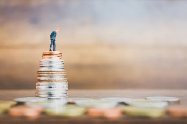 Miniature man stands on pile of coins