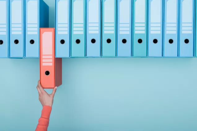 A hand taking a pink box from a row of blue boxes. Photo.