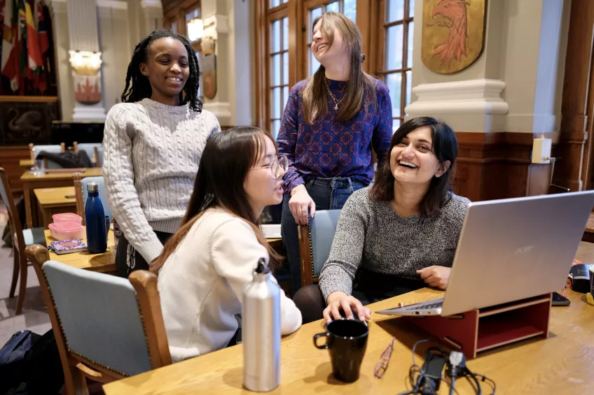 Four laughing students of different nationalities in front of a laptop. Photo. 