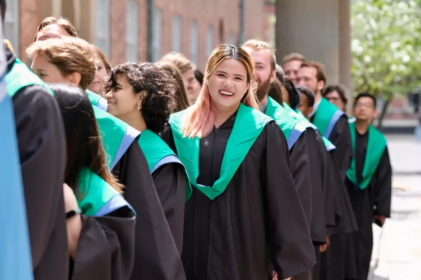 The students standing in a row with black gowns on. Photo. 