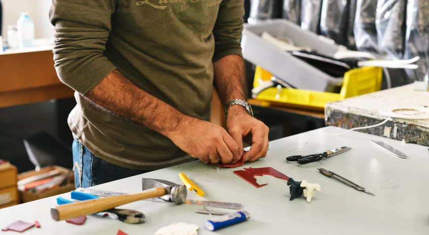 Close up of a man's arms and hands, standing by a work bench with tools 