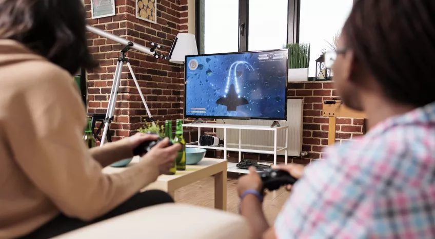 Two people are photographed from behind playing a video game 